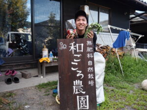 和ごころ農園さんの看板の前で、収穫野菜を持って記念撮影