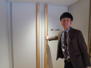 議場のドアを触る佐伯さん